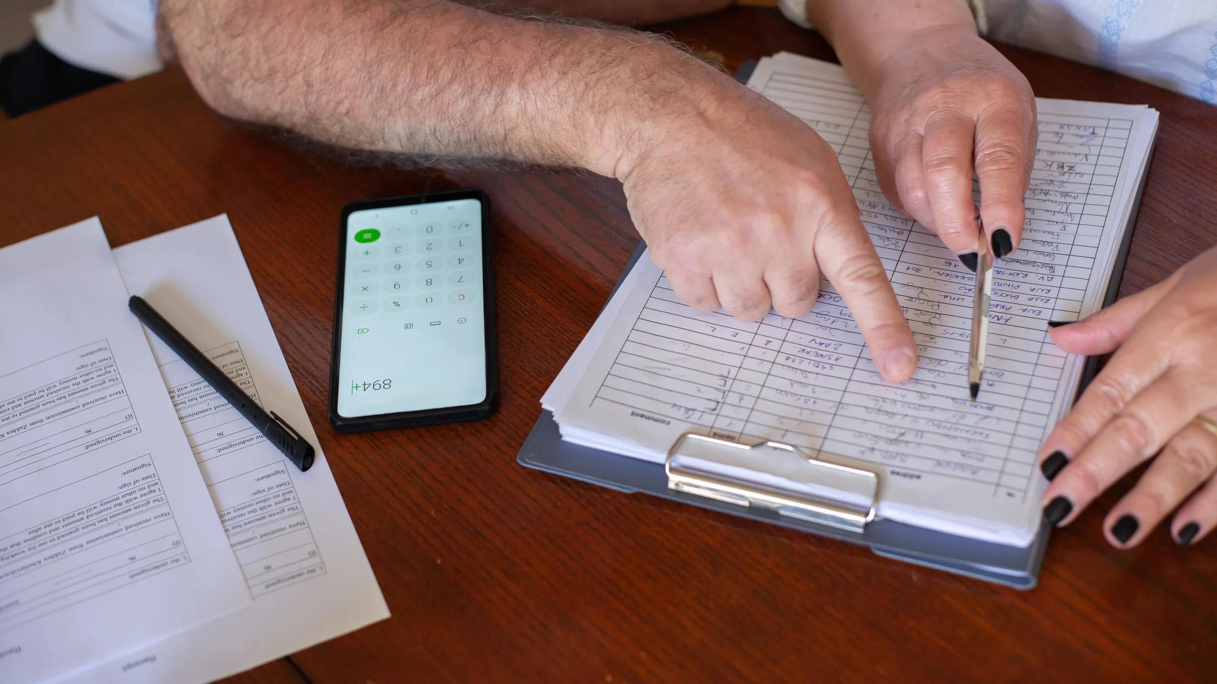 Close-up of hands working on finance planning with documents and a smartphone calculator.