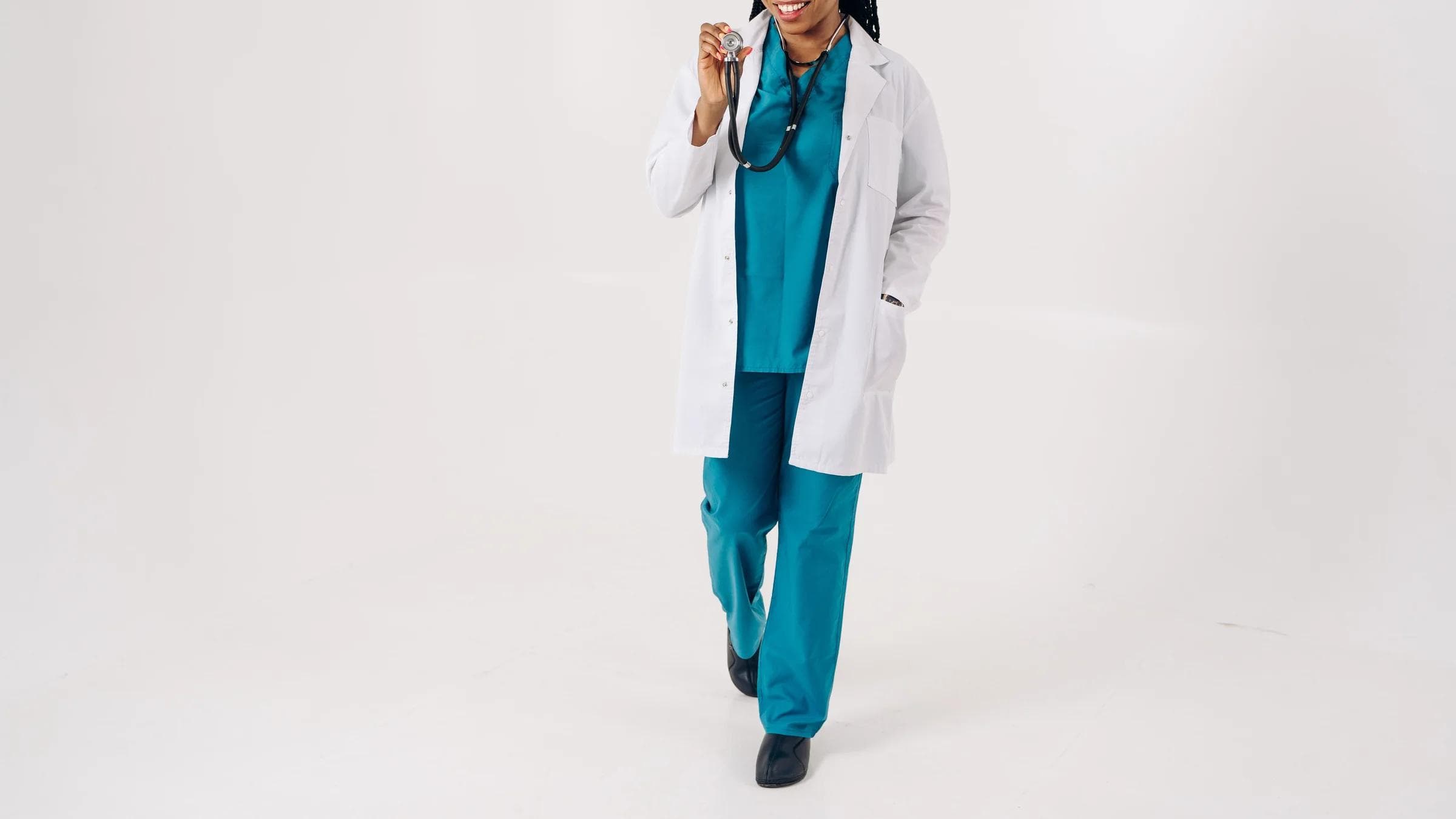 Confident female doctor in scrubs and lab coat smiling with stethoscope, studio setting.