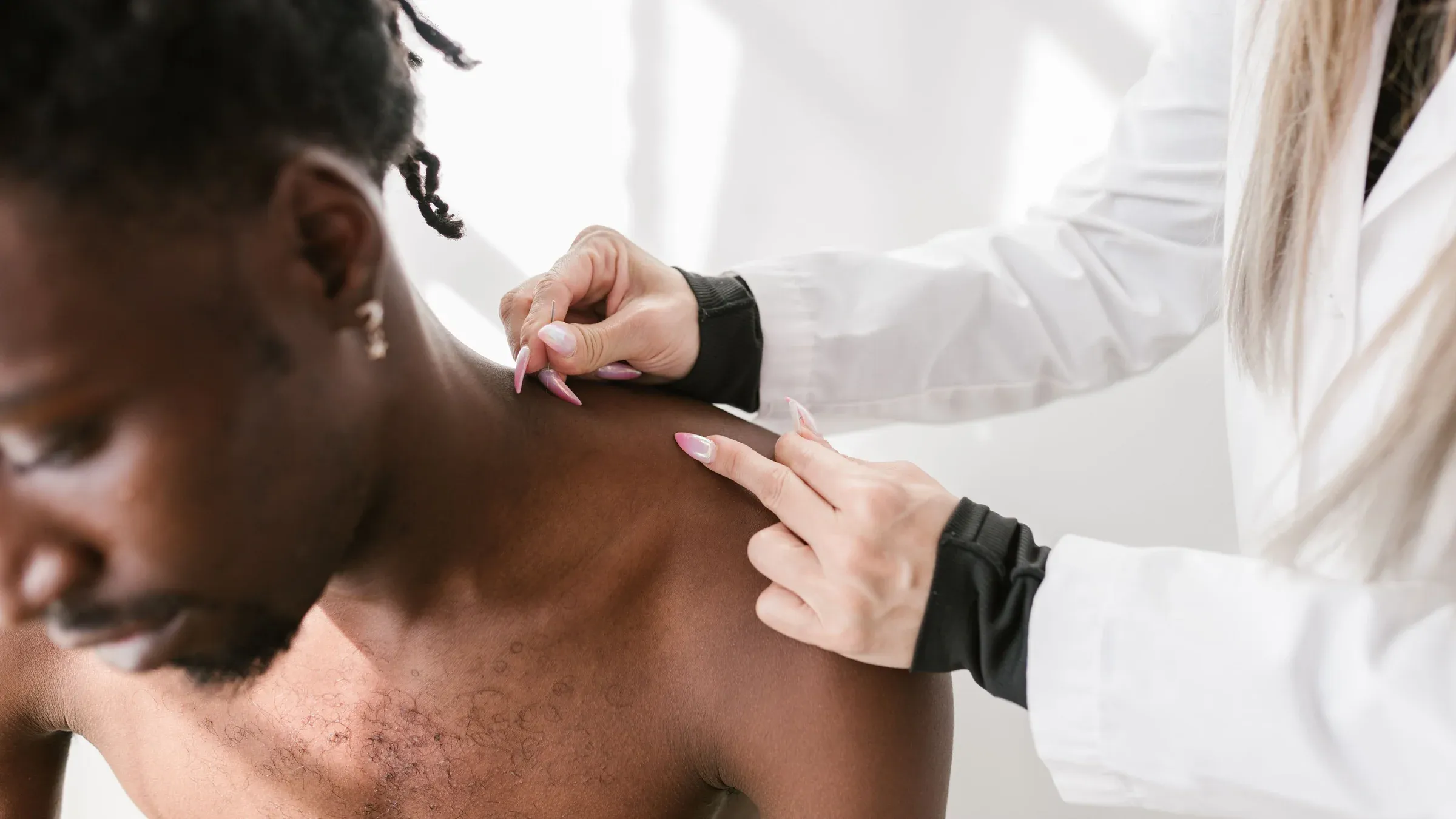 Close-up of a healthcare professional examining an adult man's shoulder in a clinical setting.