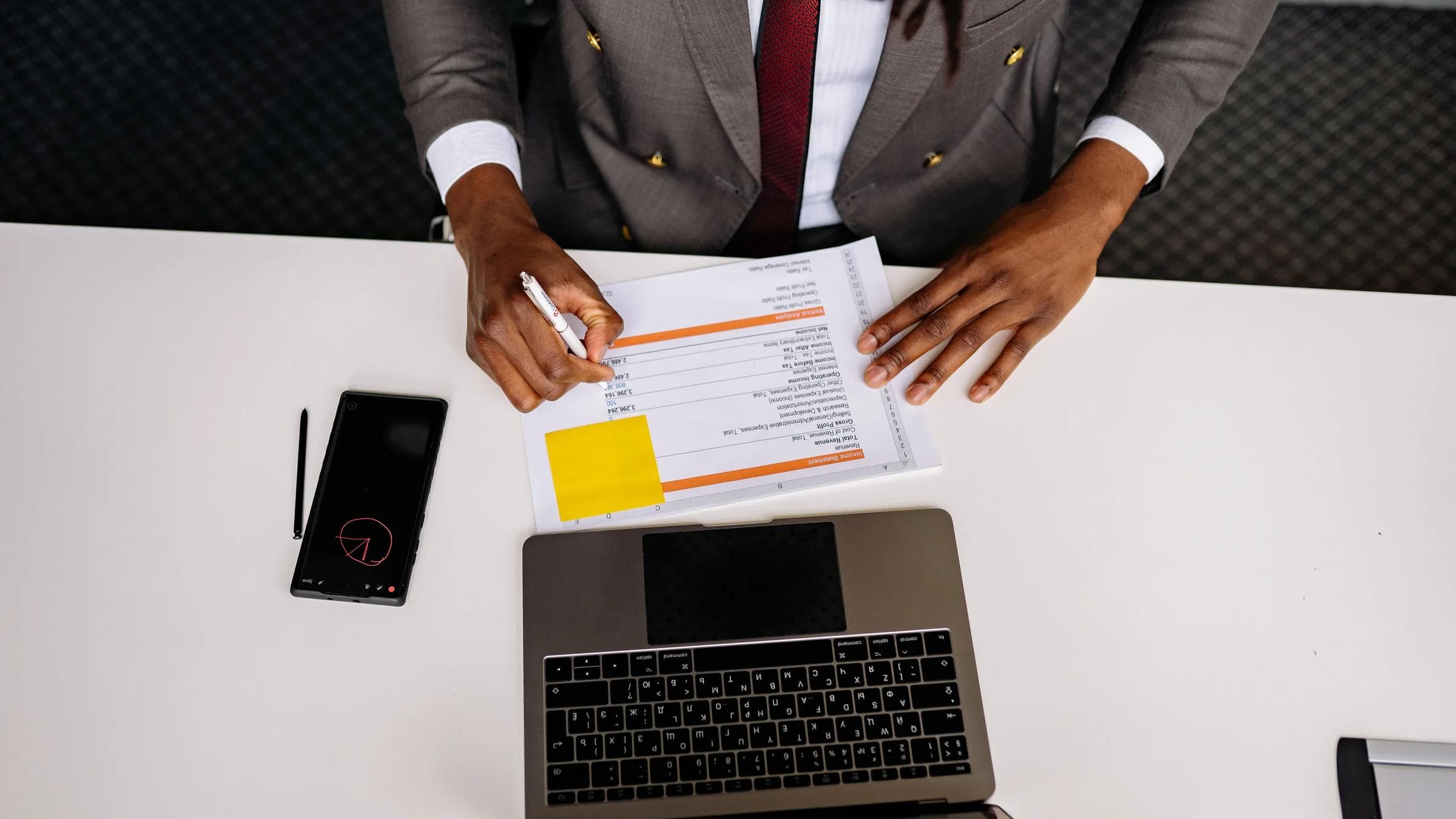 Top view of a business professional analyzing documents with a laptop on a white desk in an office setting.