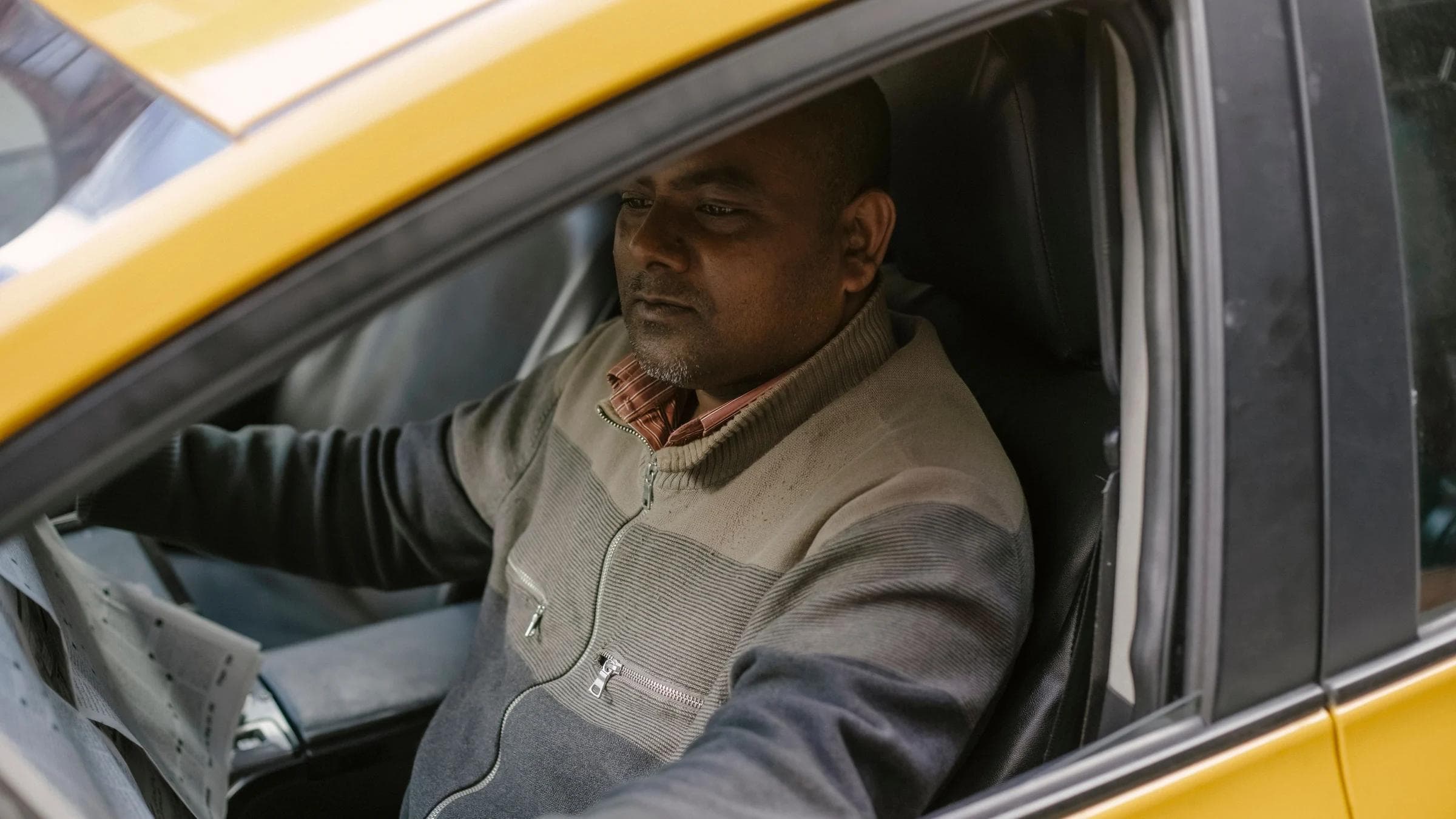 Ethnic male driver reading daily newspaper with interest while sitting in car and having break.