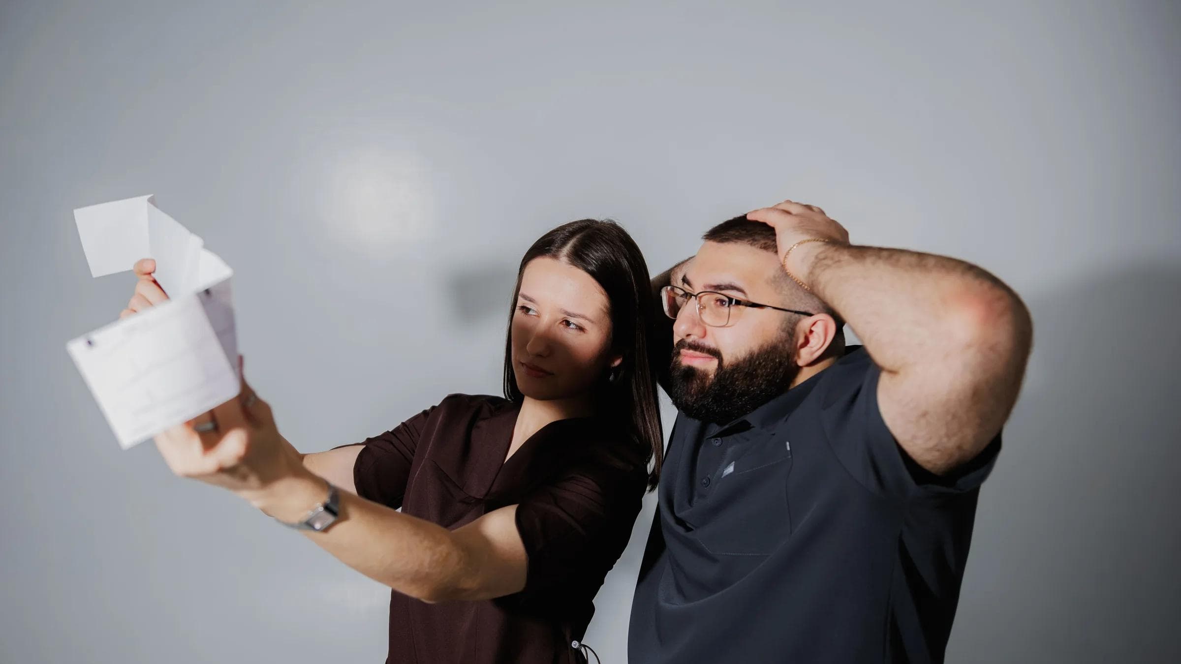 A man and woman react surprisedly while examining a document in a neutral setting.