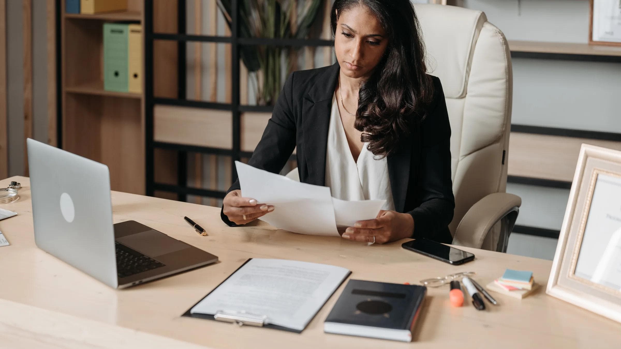 Business woman focused on paperwork at office desk, reviewing documents.