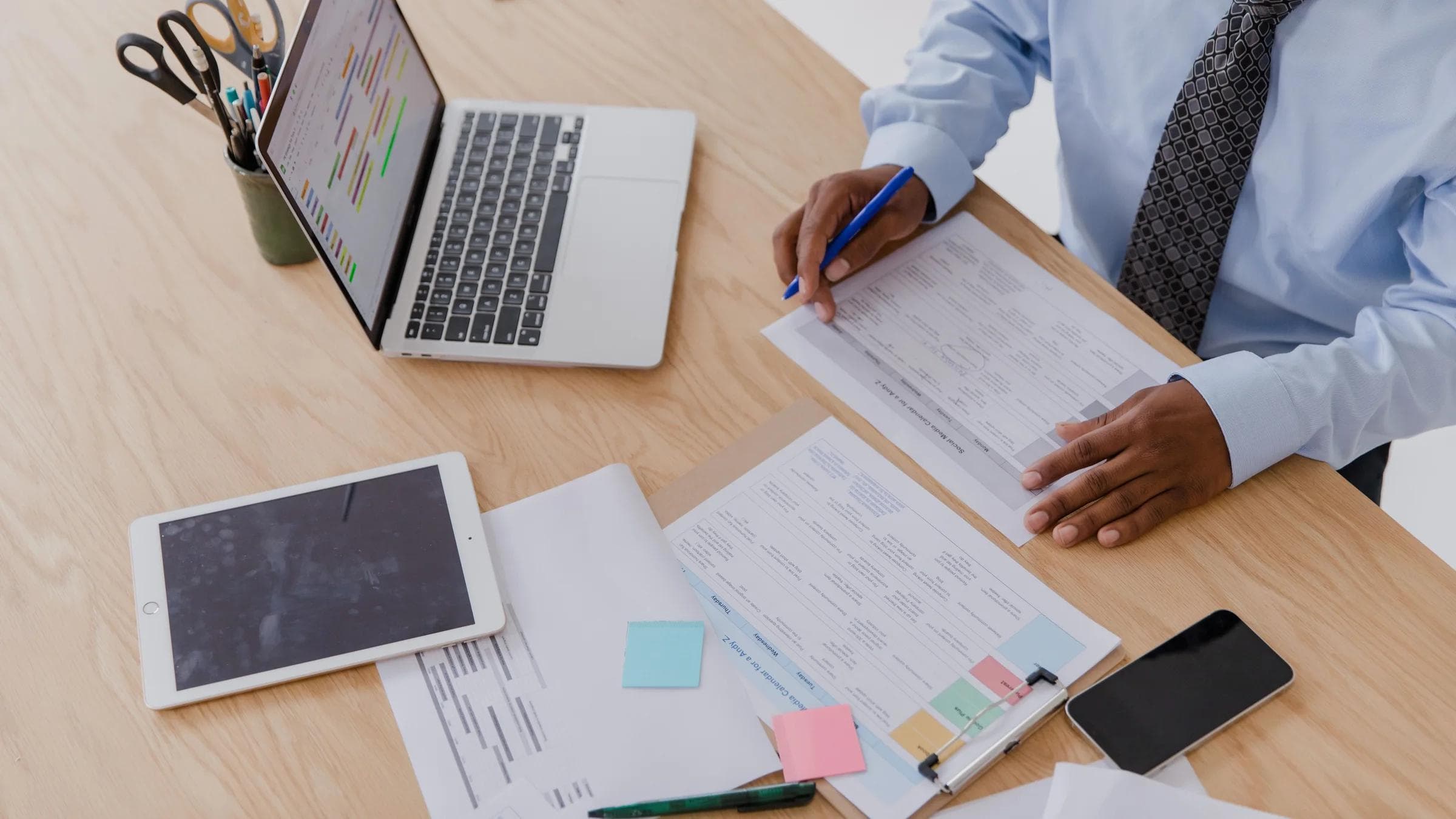 High angle view of a businessman working at a desk with a laptop, tablet, and documents.