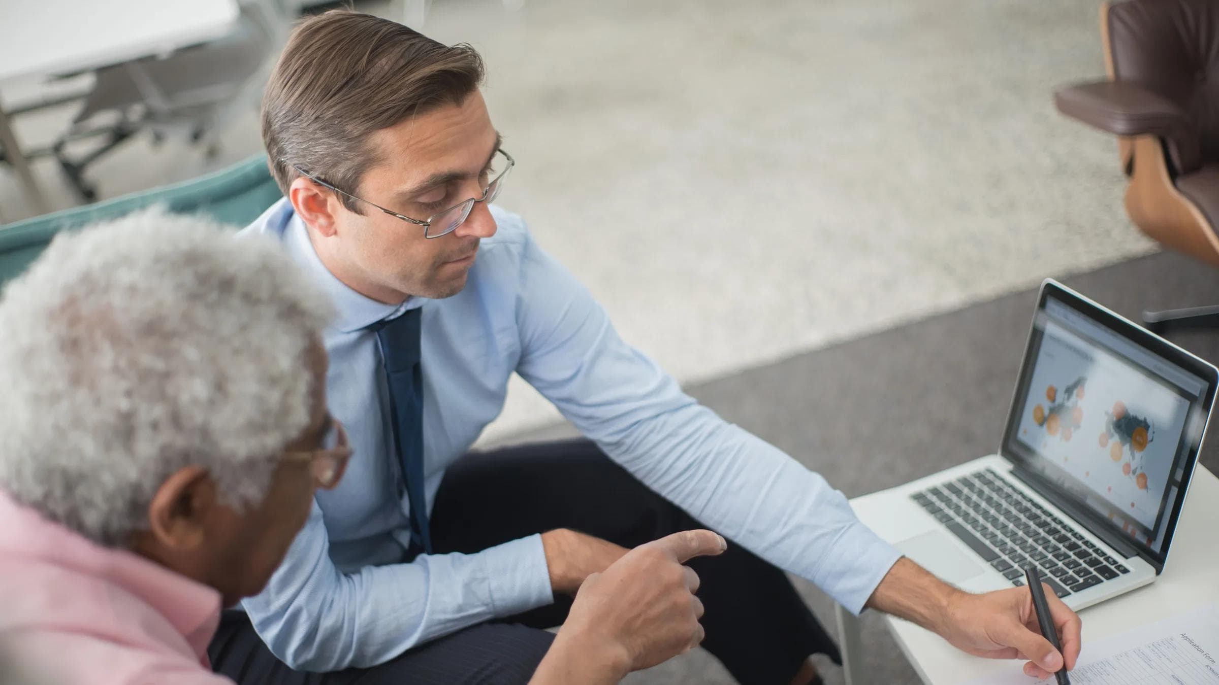 Two men in a business meeting reviewing financial documents and discussing data on a laptop.