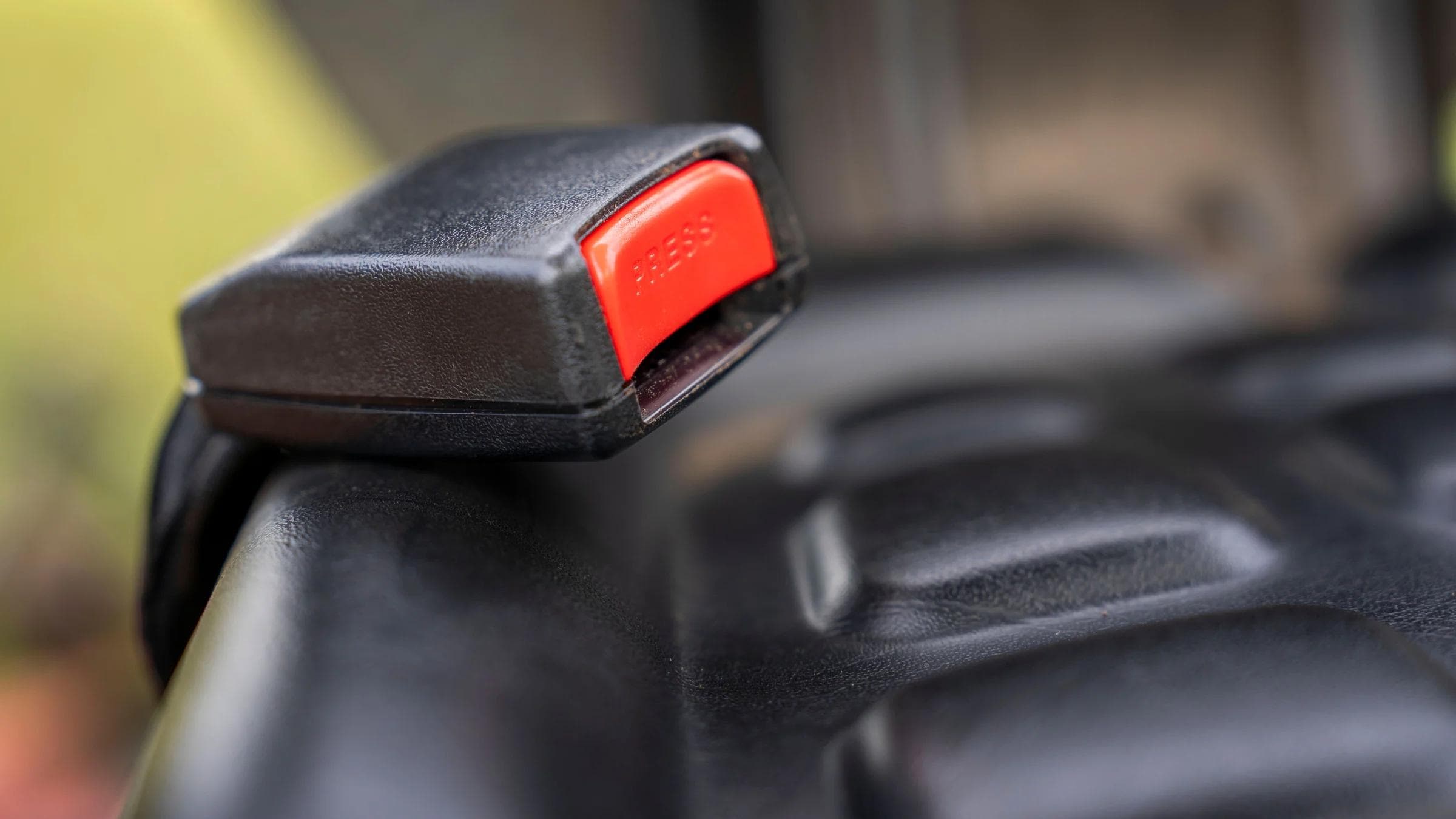 A detailed close-up image of a car seat belt buckle showing the red press button.