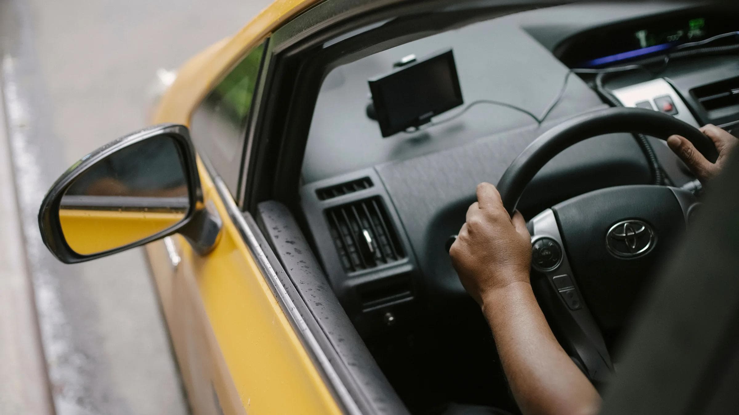 From above of crop unrecognizable person driving modern yellow taxi car with GPS navigator on city street in daytime.