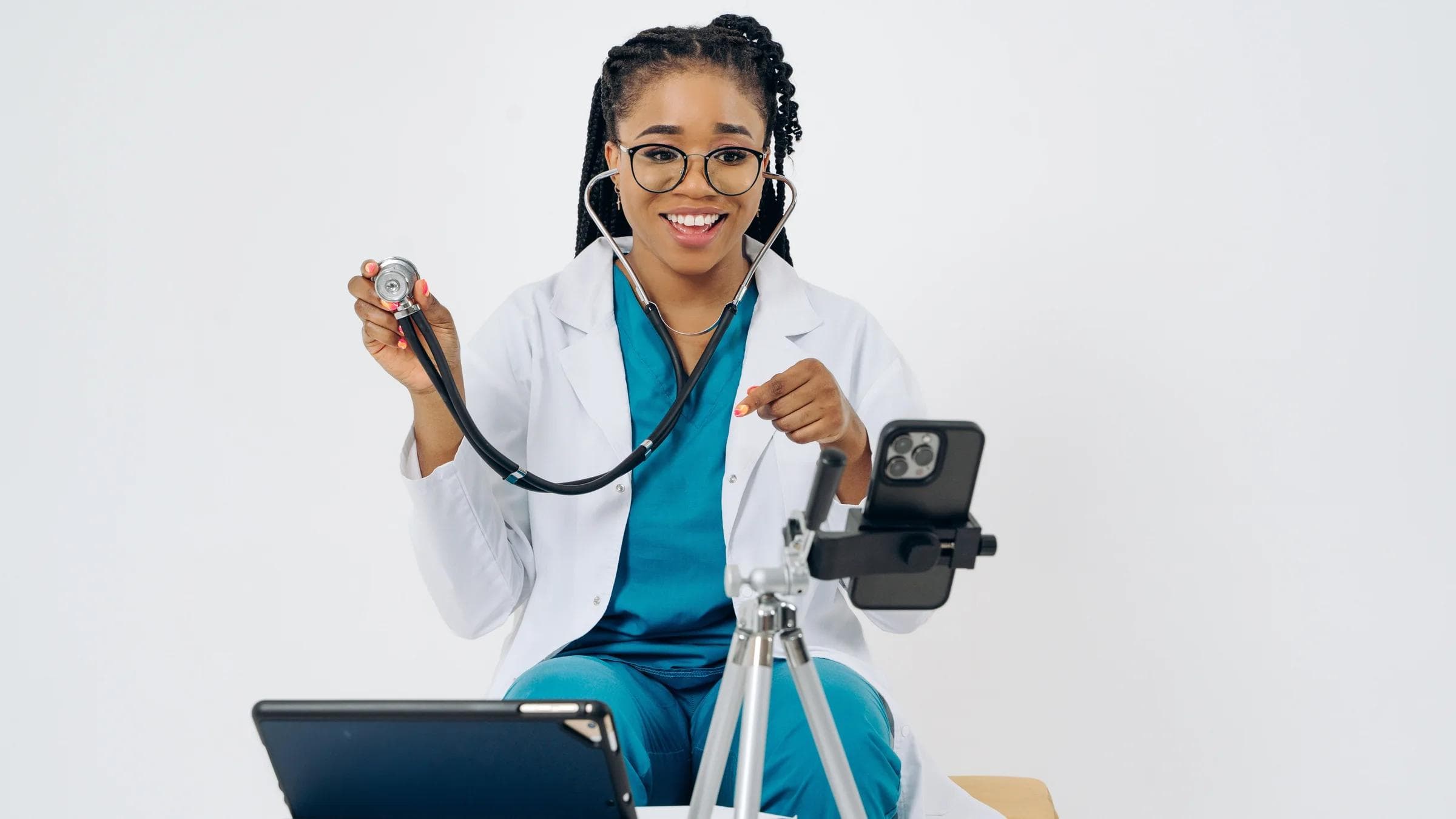 A smiling female doctor conducting a telehealth consultation using a smartphone and tablet.