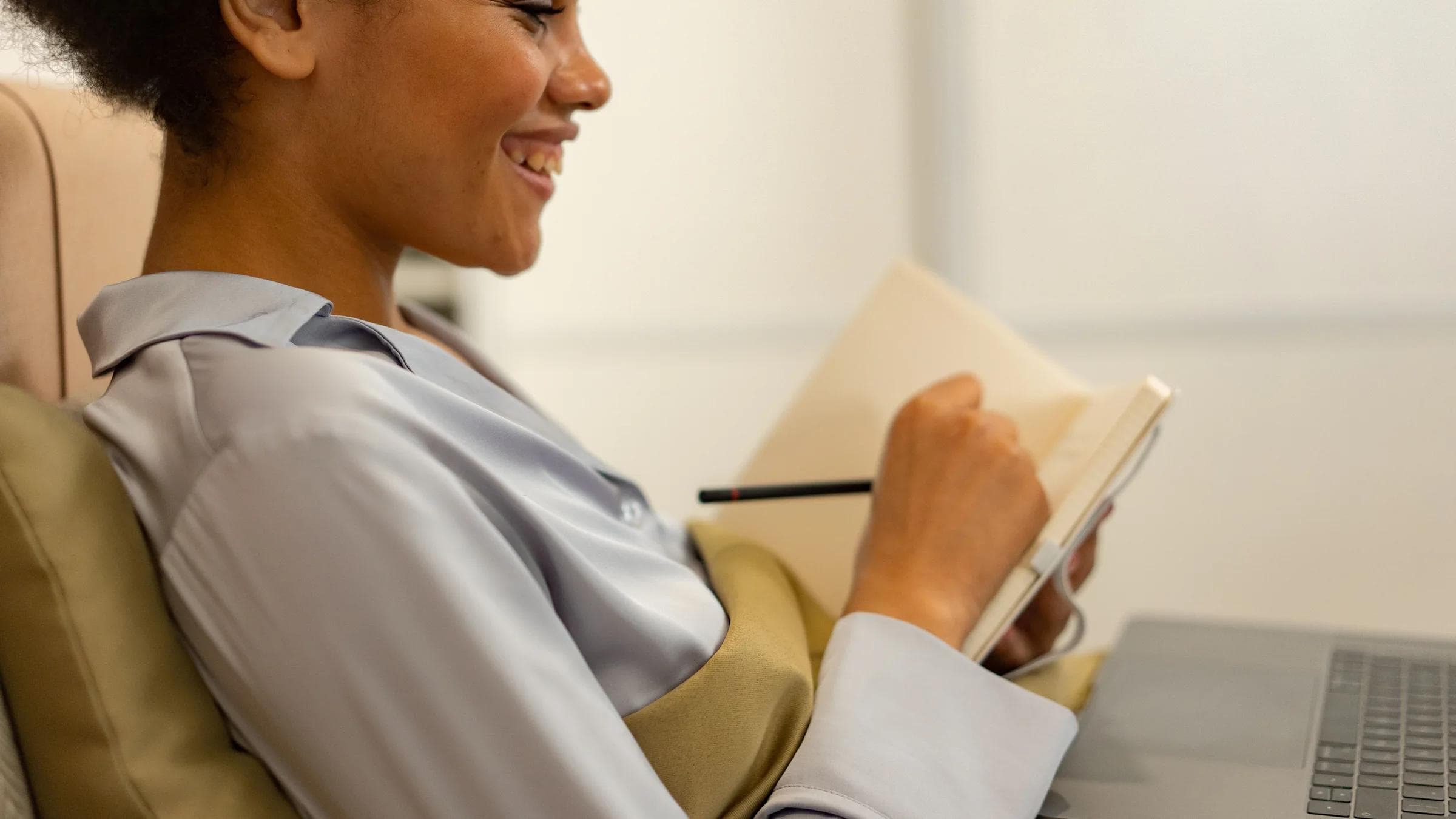Woman in pajamas studying online, writing notes in a cozy indoor setting.