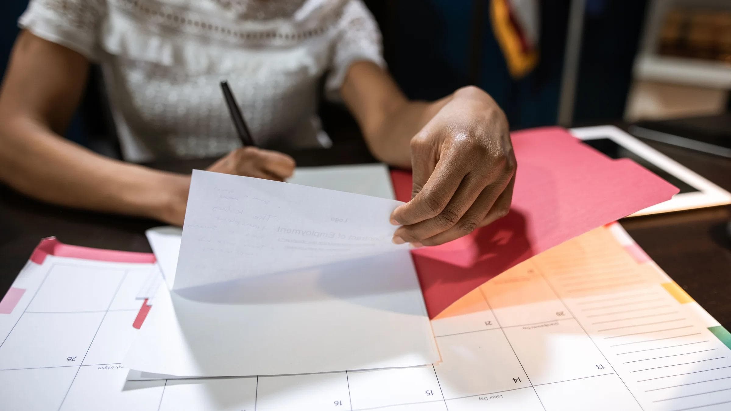 Focused woman writing and organizing papers at a desk with a calendar.