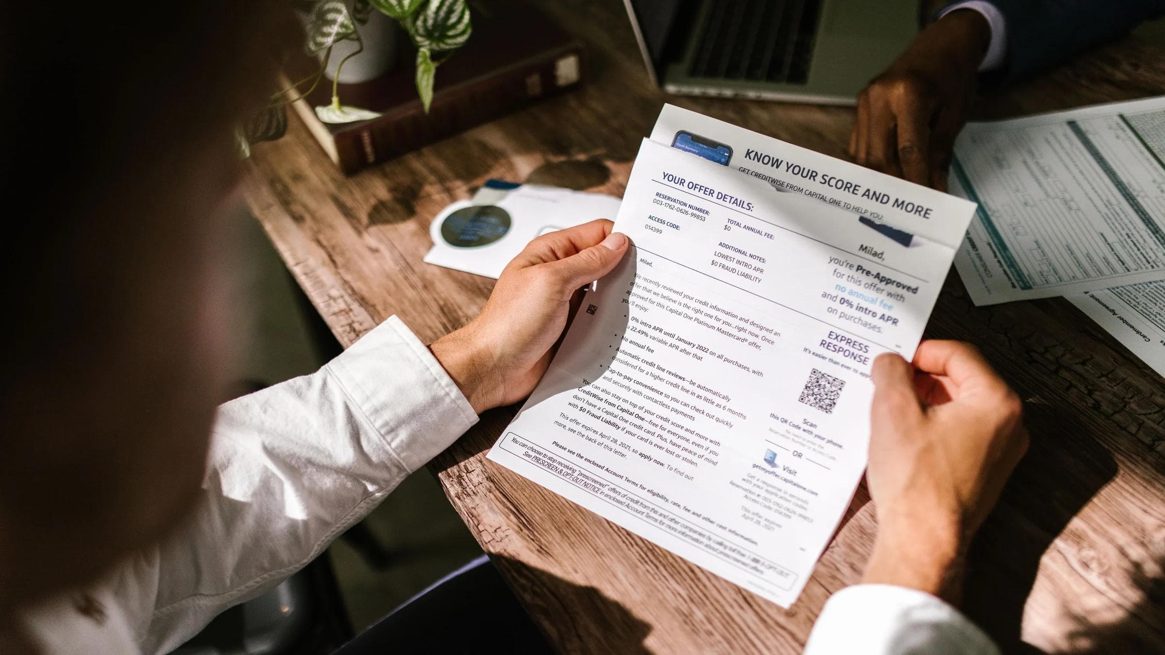 An adult man examining a financial document under natural light at a wooden desk, emphasizing finance and reading.