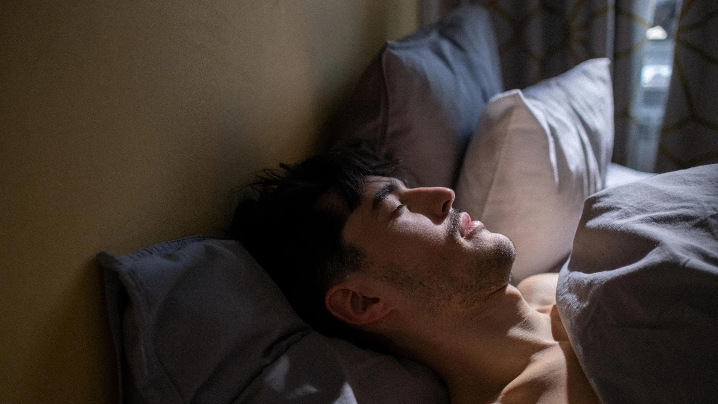 A man peacefully sleeping in bed with gentle morning light streaming in a cozy bedroom.