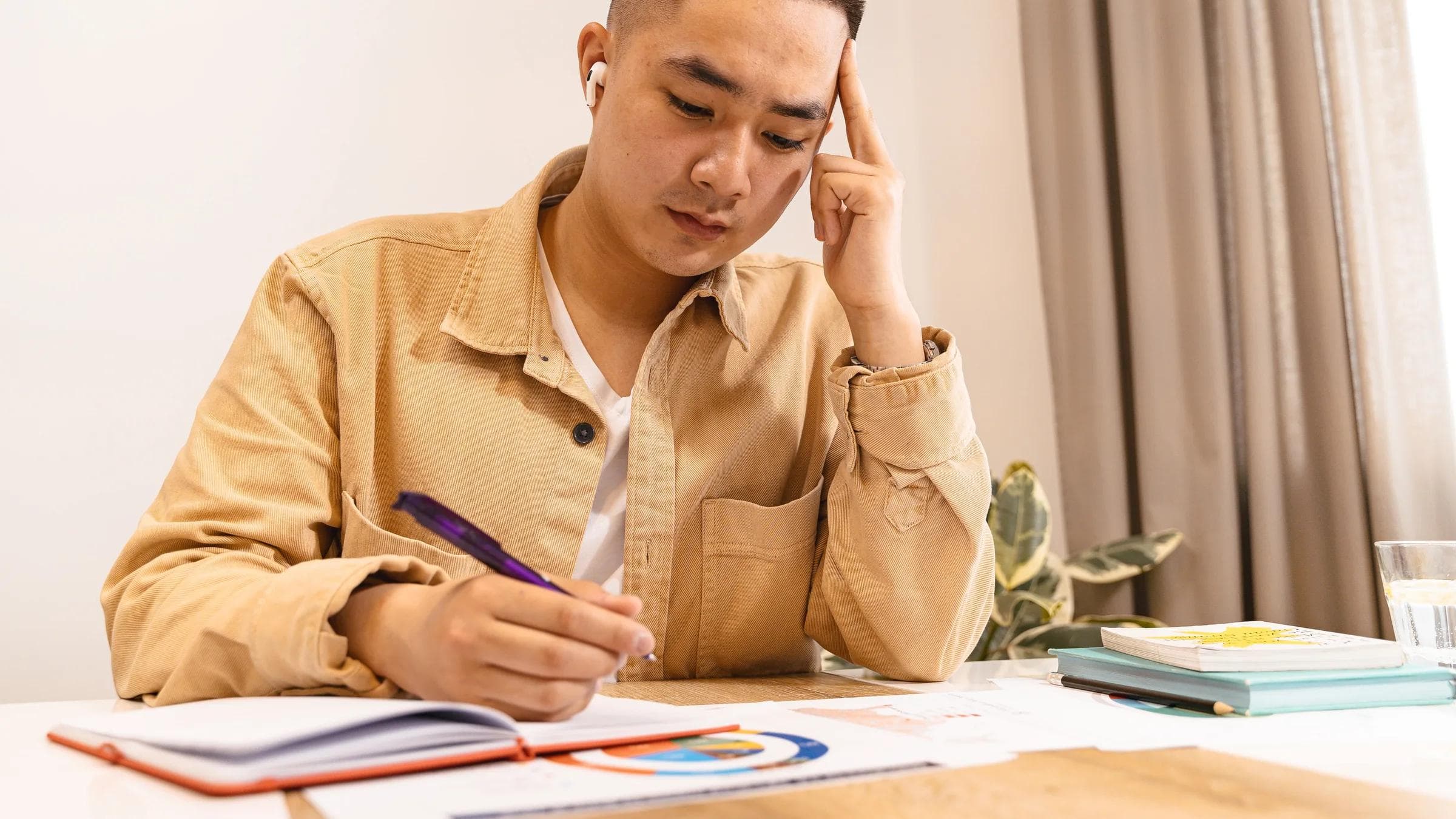 Young adult deeply focused on studying with earphones, writing notes at a desk.