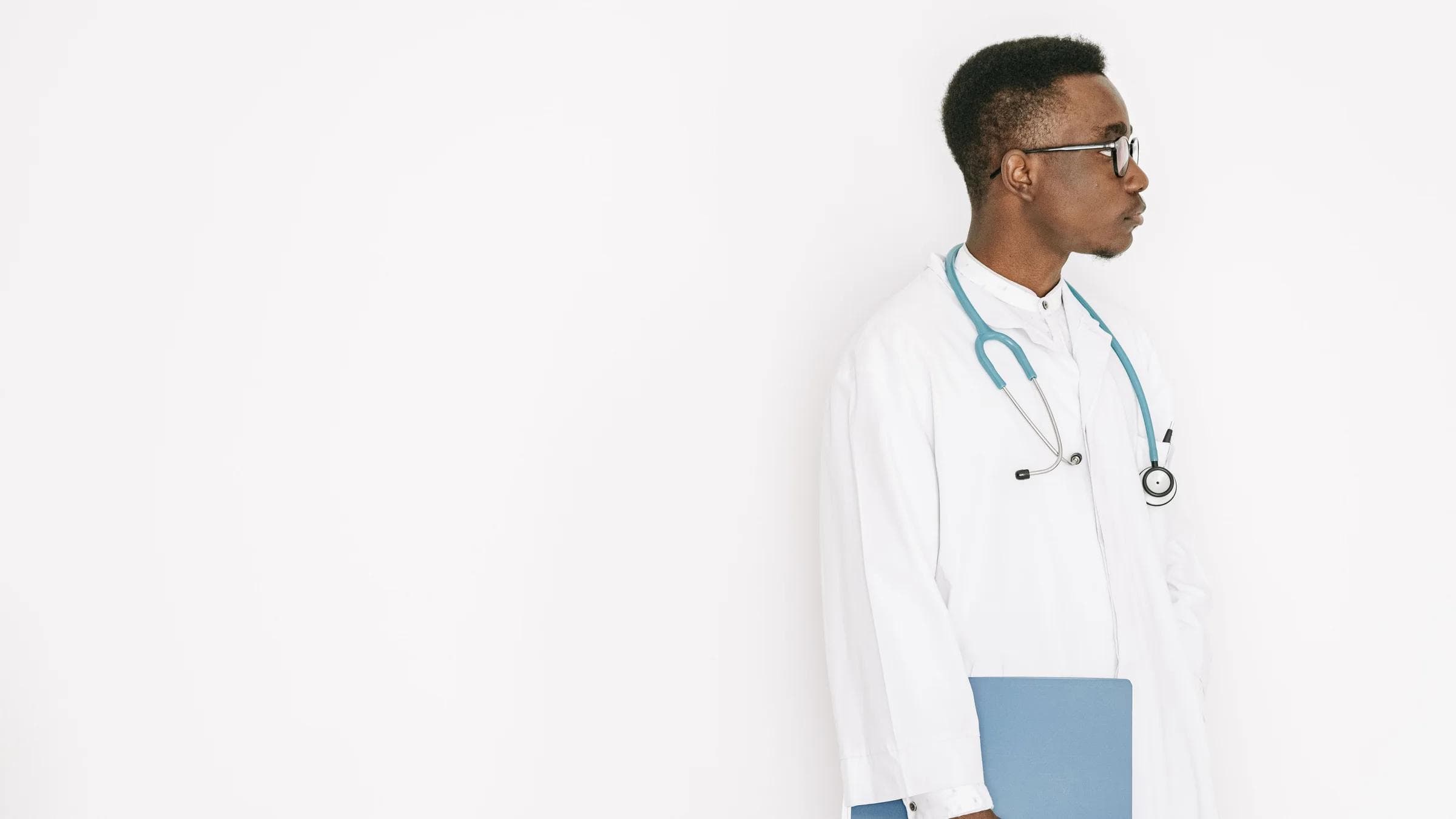 Side profile of a doctor in a medical gown holding a folder with a stethoscope around the neck.