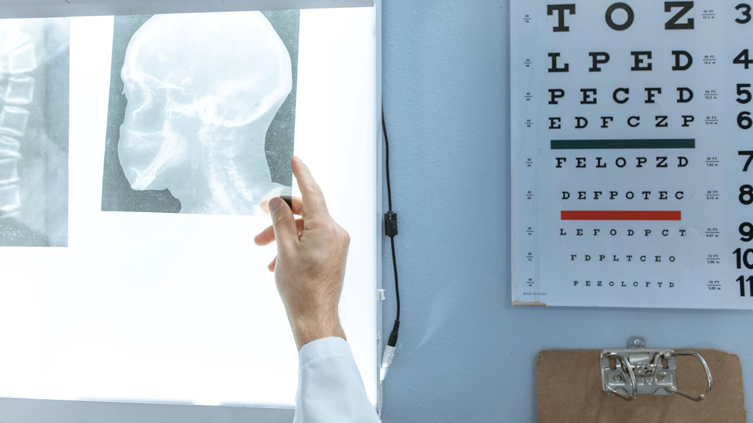 A medical professional checks an X-ray next to a Snellen eye chart in a clinic.